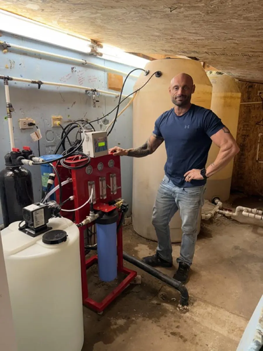 Technician beside a reverse osmosis system and storage tank in a basement
