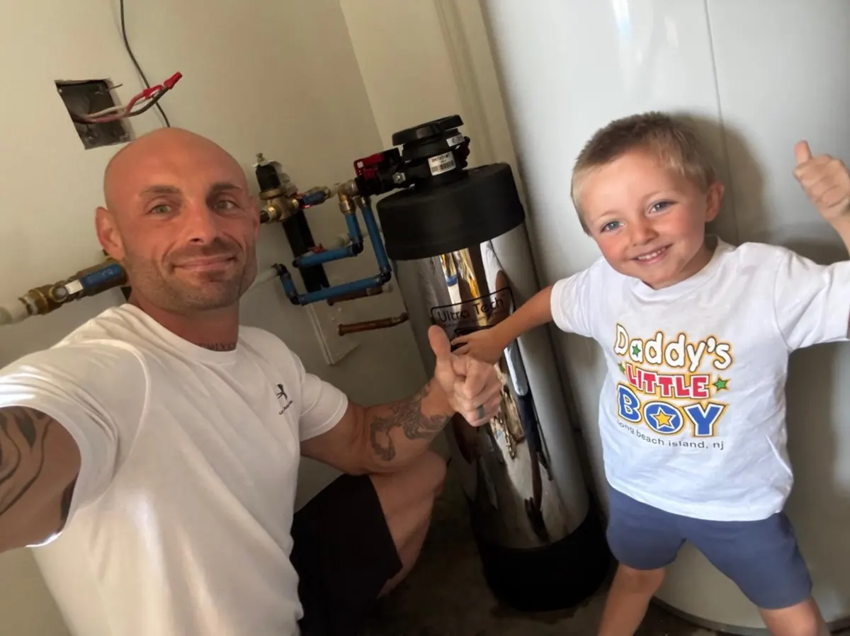 Technician and a young helper with a stainless whole-home system after installation