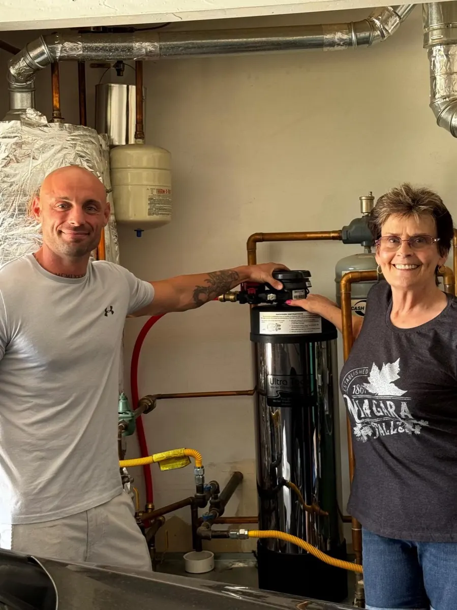Technician and homeowner with a stainless whole-home filter in the utility room